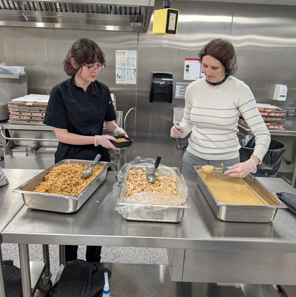 Two people making food in a school kitchen